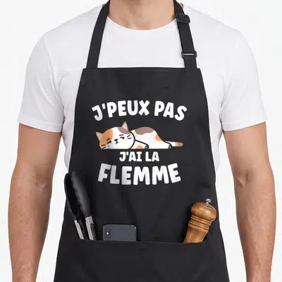 Tablier de cuisine noir avec un chat tricolore endormi et le texte J'peux pas j'ai la flemme imprimé en blanc.