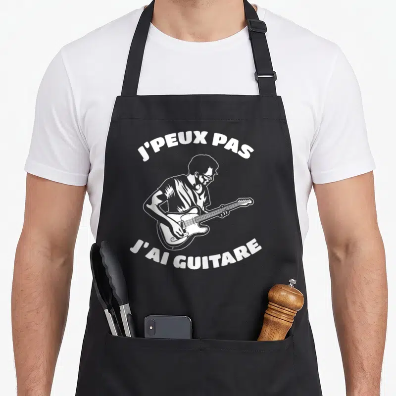 Tablier de cuisine noir avec illustration d'un guitariste et le texte j'peux pas j'ai guitare en blanc.