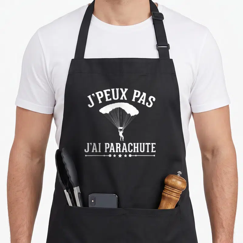 Tablier de cuisine noir avec l'illustration blanche d'un parachutiste et la citation J'peux pas j'ai parachute.