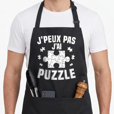Tablier de cuisine noir avec inscription blanche J'peux pas j'ai puzzle et illustration de pièces de jeu.