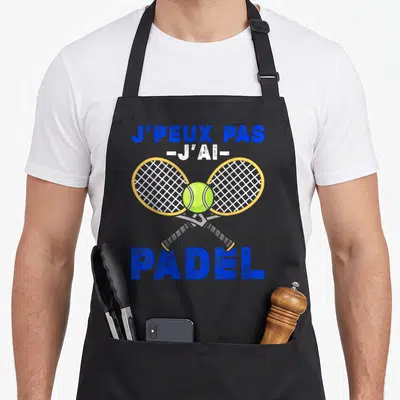 Tablier de cuisine noir avec deux raquettes de padel croisées et une balle jaune au centre.