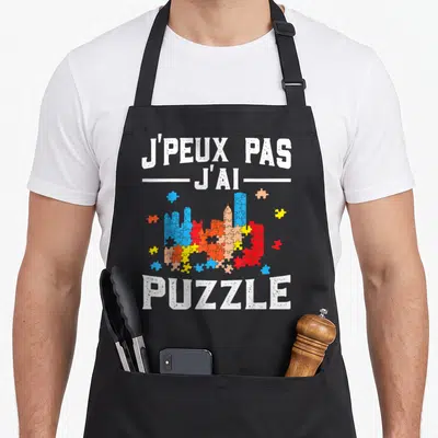 Tablier de cuisine noir avec inscription j'peux pas j'ai puzzle et illustration de pièces multicolores.