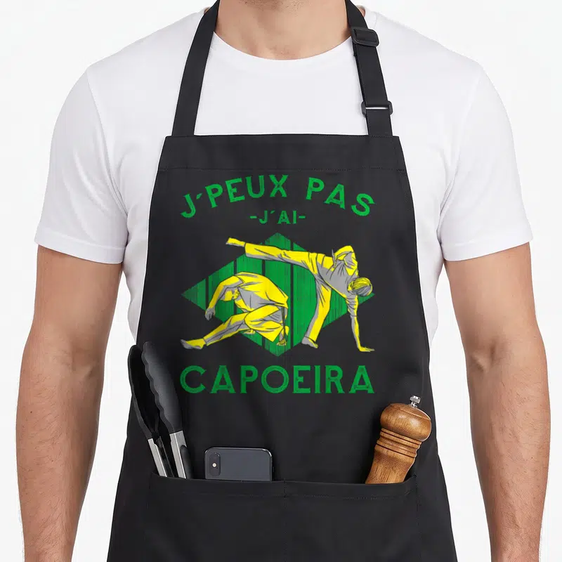 Tablier de cuisine noir avec deux silhouettes effectuant des mouvements de capoeira sous un texte vert.