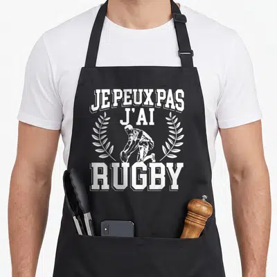 Tablier de cuisine noir avec inscription je peux pas j'ai rugby et illustration de joueur agenouillé encadré par des branches de laurier.