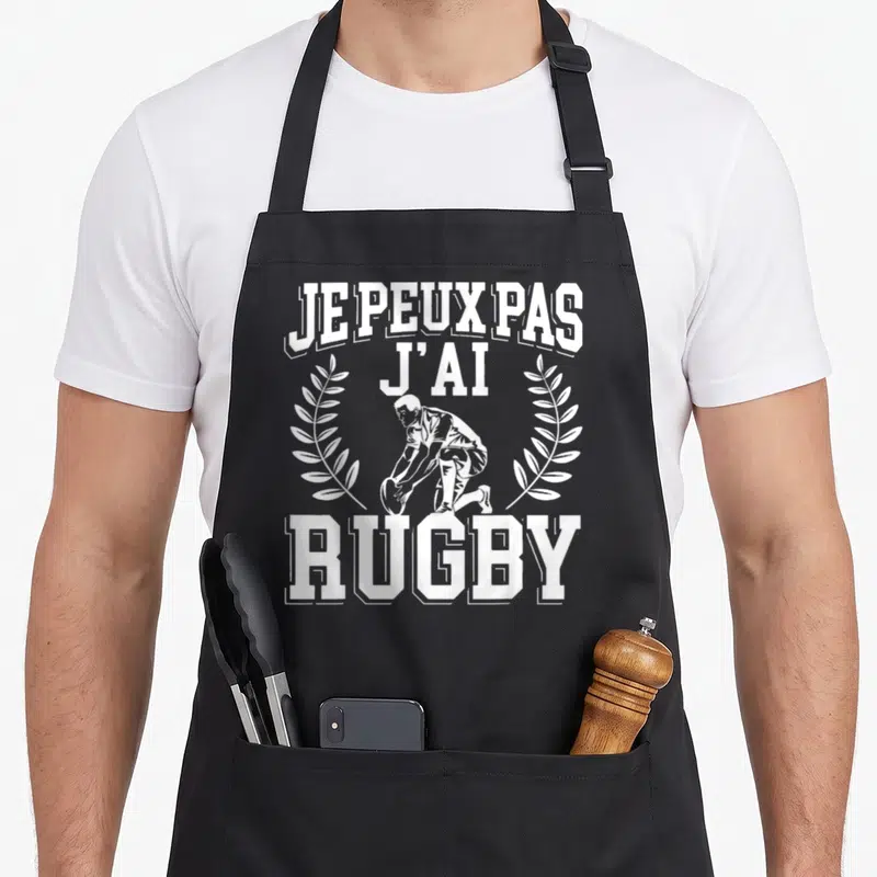 Tablier de cuisine noir avec inscription je peux pas j'ai rugby et illustration de joueur agenouillé encadré par des branches de laurier.