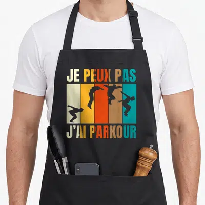 Tablier de cuisine noir avec texte je peux pas j'ai parkour et silhouettes de sauts sur fond de bandes colorées.