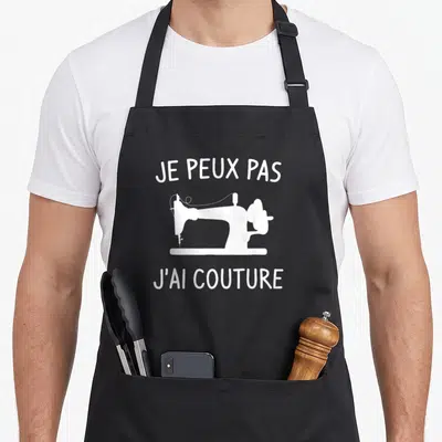 Tablier de cuisine noir avec texte je peux pas j'ai couture et silhouette de machine à coudre blanche.