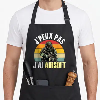 Tablier de cuisine noir avec illustration d'un joueur de soft air tenant un fusil devant un soleil coloré.