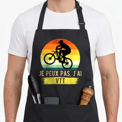 Tablier de cuisine noir avec silhouette cycliste VTT et texte Je peux pas j'ai VTT sur fond de soleil rayé.