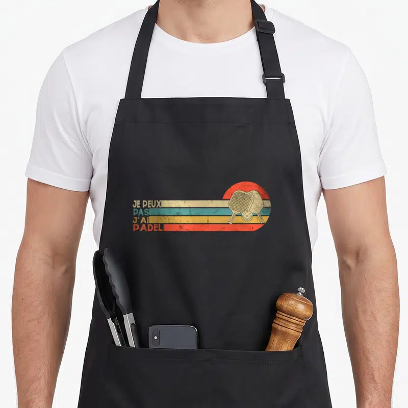 Tablier de cuisine noir avec inscription je peux pas j'ai Padel et deux raquettes sur bandes colorées rétro.