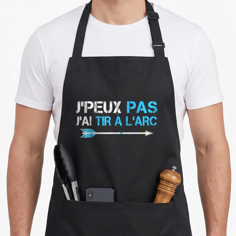 Tablier de cuisine noir avec le texte JPEUX PAS JAI TIR A LARC et une flèche bleue blanche imprimée au centre.