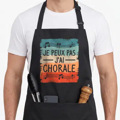 Tablier de cuisine noir avec motif coloré affichant je peux pas j'ai chorale et des notes de musique.