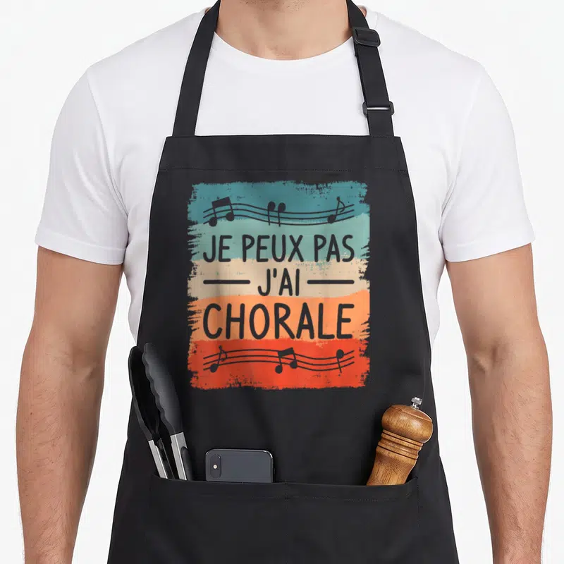 Tablier de cuisine noir avec motif coloré affichant je peux pas j'ai chorale et des notes de musique.