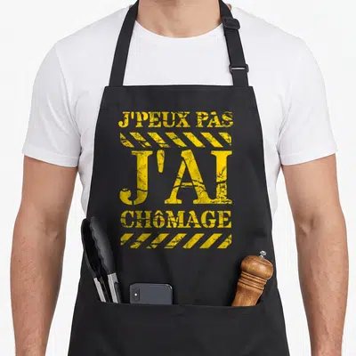 Tablier de cuisine noir avec inscription jaune J'PEUX PAS J'AI CHÔMAGE et motifs de bandes de signalisation.