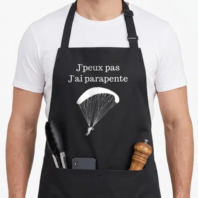 Tablier de cuisine noir avec inscription J'peux pas j'ai parapente et silhouette de voilier blanche