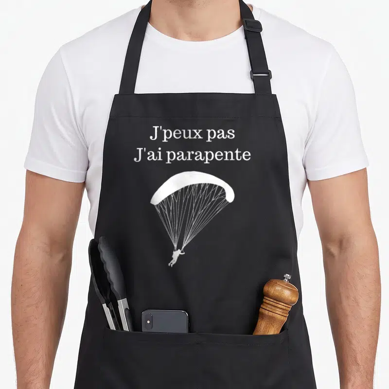 Tablier de cuisine noir avec inscription J'peux pas j'ai parapente et silhouette de voilier blanche