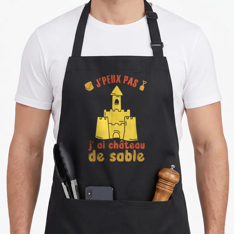 Tablier de cuisine noir avec illustration jaune château de sable et texte orange J'peux pas j'ai château de sable été