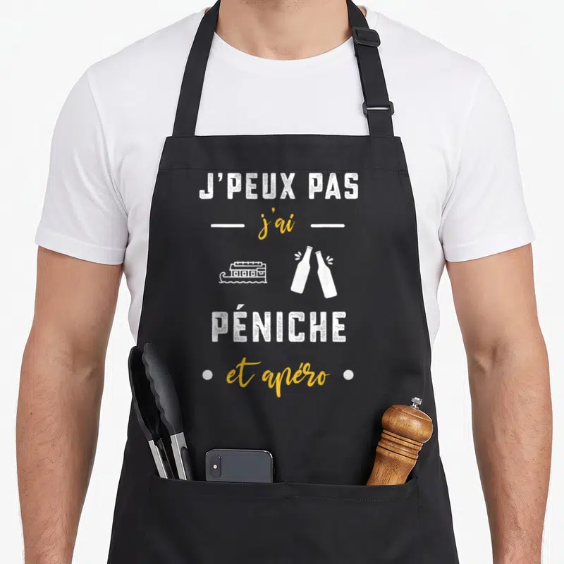 Tablier de cuisine noir avec l'inscription J'peux pas j'ai péniche et apéro accompagnée d'un dessin de bateau et de bouteilles.