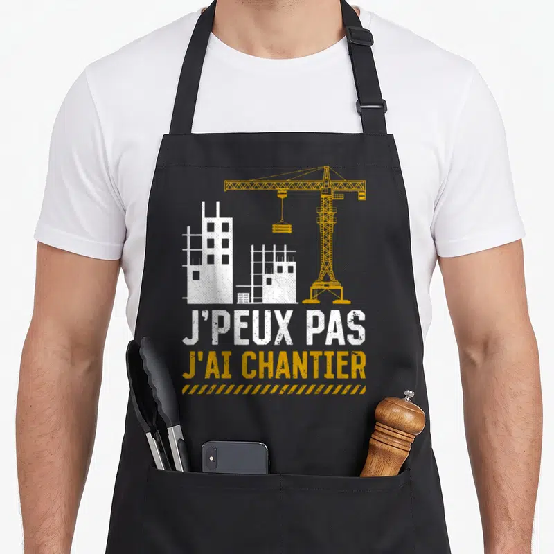 Tablier de cuisine noir avec illustration de grue jaune, bâtiments blancs et texte J'PEUX PAS J'AI CHANTIER.