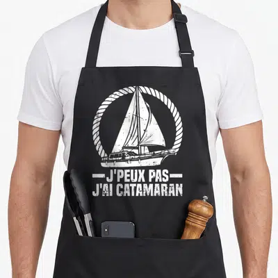 Tablier de cuisine noir avec illustration de catamaran et texte J'peux pas j'ai catamaran capitaine en blanc.