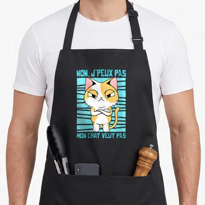 Tablier de cuisine noir avec illustration d'un chat tricolore aux bras croisés et texte bleu.