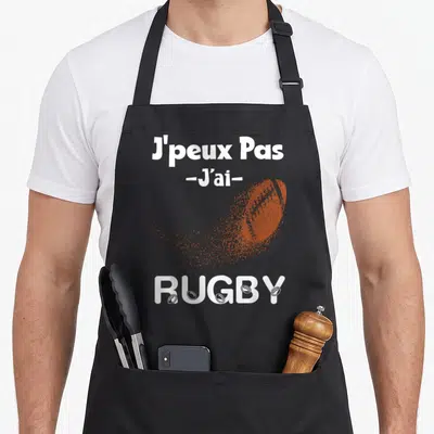 Tablier de cuisine noir avec l'inscription Je Peux Pas J'ai Rugby et un ballon orange stylisé.