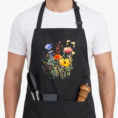Tablier de cuisine noir avec illustration colorée de fleurs sauvages d'été incluant pavots orange et fleurs bleues en aquarelle.