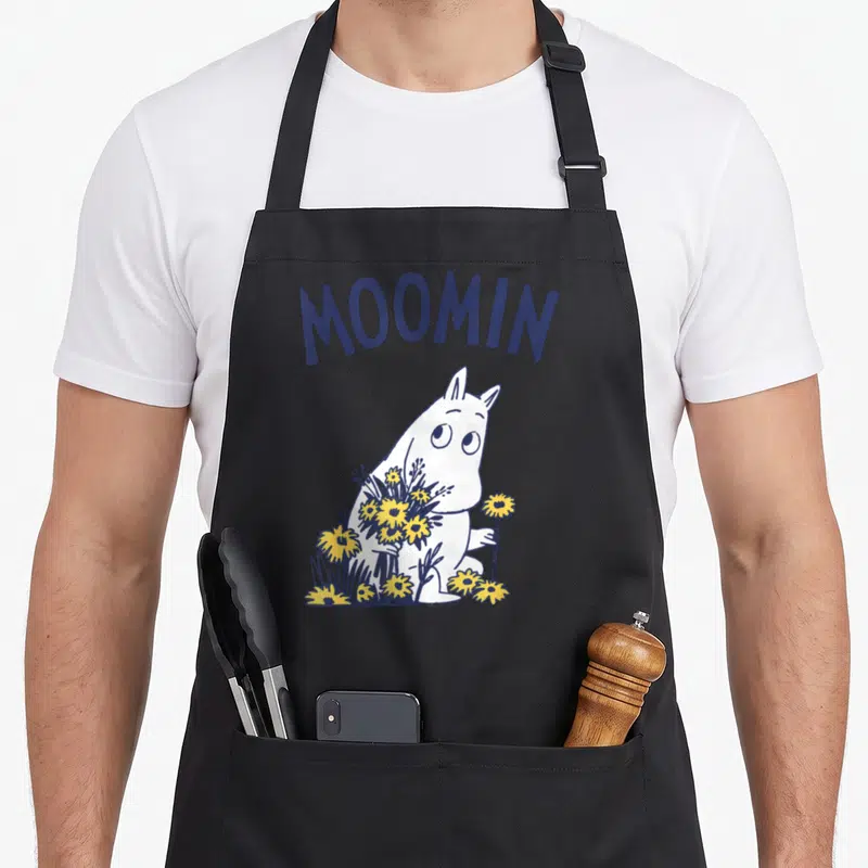 Tablier de cuisine noir avec Moomintroll tenant des fleurs jaunes et le texte Moomin en bleu marine.