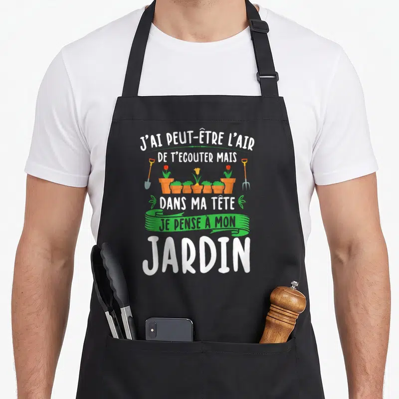 Tablier de cuisine noir avec le texte J'ai peut-être l'air de t'écouter mais dans ma tête je pense à mon jardin et des outils de jardinage.