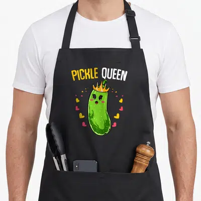 Tablier de cuisine noir avec un concombre vert muni d'une couronne jaune et le texte Pickle Queen au-dessus.