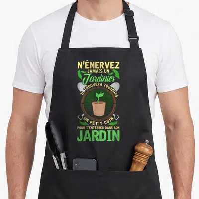 Tablier de cuisine noir avec une plante verte en pot, une bêche grise et texte jaune vert sur fond uni.