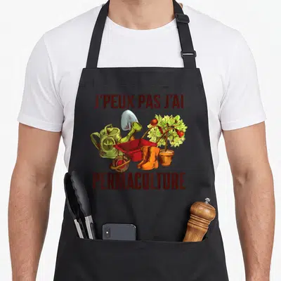 Tablier de cuisine noir avec illustration de brouette rouge, bottes orange et texte J'peux pas j'ai permaculture en lettres marron.