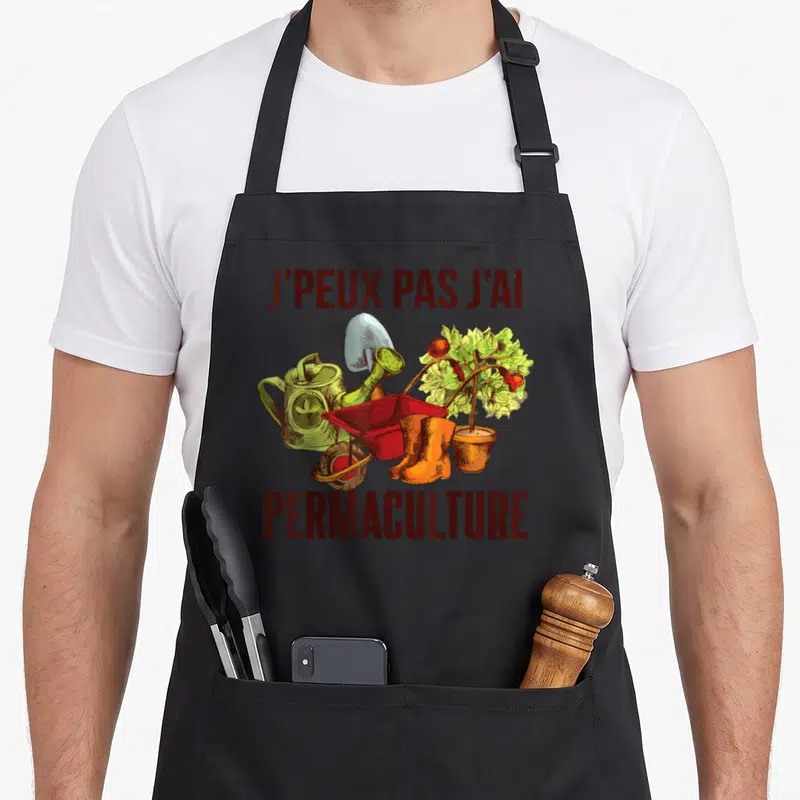 Tablier de cuisine noir avec illustration de brouette rouge, bottes orange et texte J'peux pas j'ai permaculture en lettres marron.