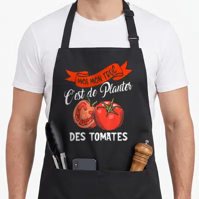 Tablier de cuisine noir avec une bannière rouge, du texte blanc et deux tomates rouges entières et coupées.