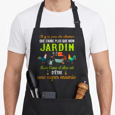 Tablier de cuisine noir avec inscription que j'aime plus que mon jardin super mamie entouré de coqs et d'outils de potager colorés.