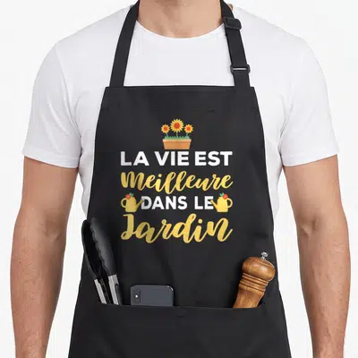 Tablier de cuisine noir avec inscription La vie est meilleure dans le jardin et illustrations de fleurs et d'arrosoirs jaunes.
