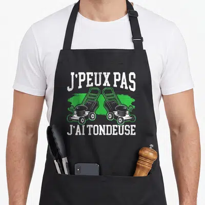Tablier de cuisine noir avec deux tondeuses grises et le texte J'peux pas j'ai tondeuse en blanc.