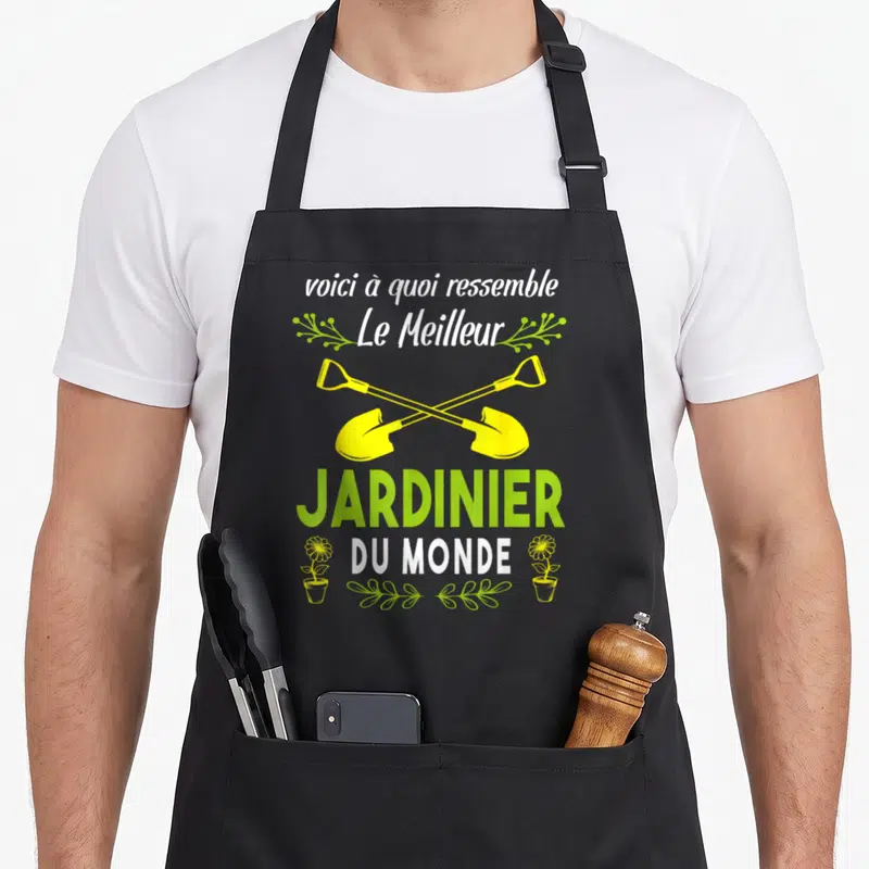 Tablier de cuisine noir avec inscription Voici à quoi ressemble le meilleur jardinier du monde et deux pelles jaunes croisées.
