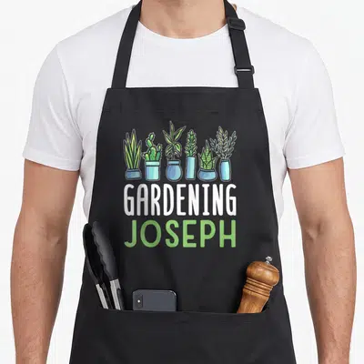 Tablier de cuisine noir avec six plantes en pots bleus et les mots Gardening Joseph en blanc et vert.