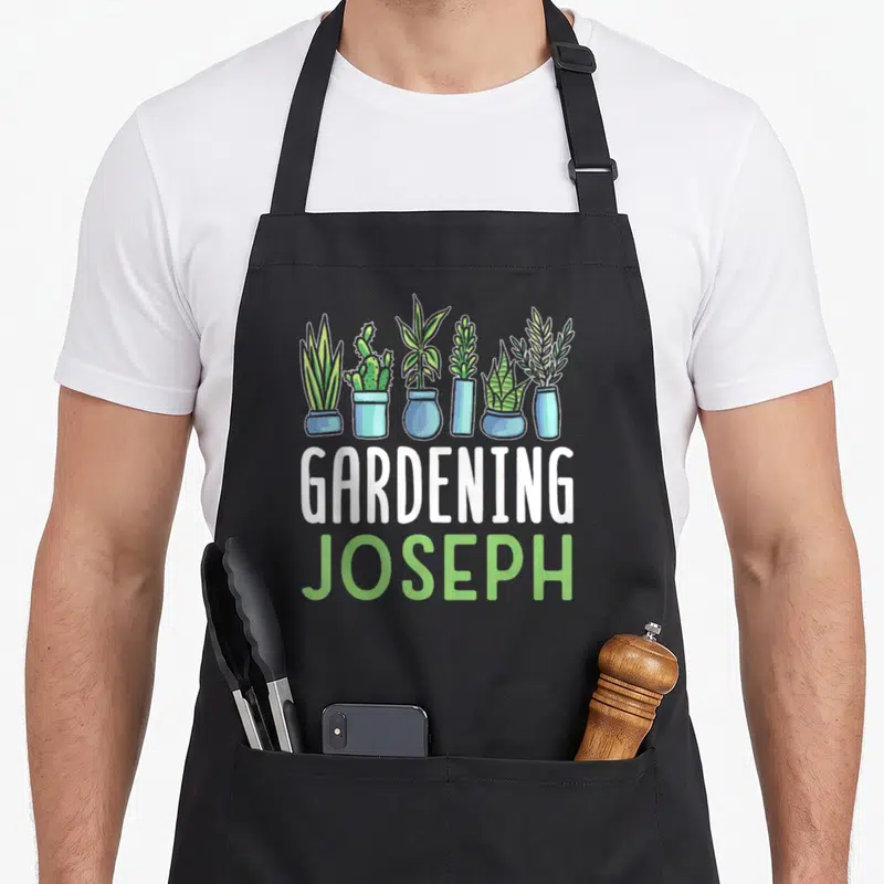 Tablier de cuisine noir avec six plantes en pots bleus et les mots Gardening Joseph en blanc et vert.