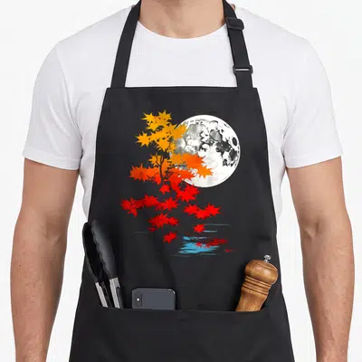 Tablier de cuisine noir avec illustration d'une lune grise et de feuilles d'érable rouges et oranges se reflétant dans l'eau.