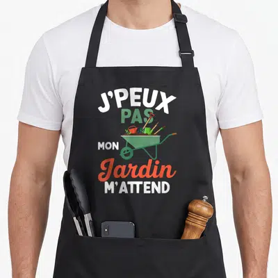 Tablier de cuisine noir avec une illustration de brouette verte et le texte J'peux pas mon Jardin m'attend