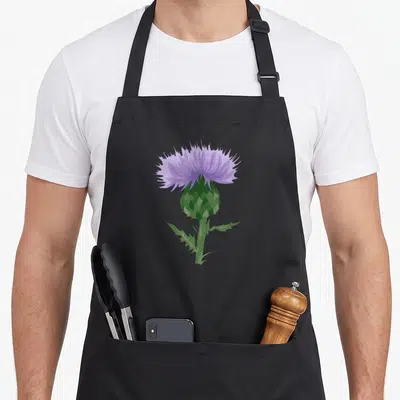 Tablier de cuisine noir avec illustration centrale d'une fleur de chardon écossais violette et de ses feuilles épineuses vertes.