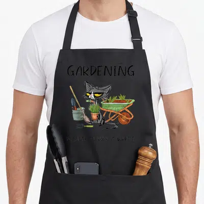 Tablier de cuisine noir avec un chat gris aux yeux jaunes tenant une plante et une brouette pleine de verdure.