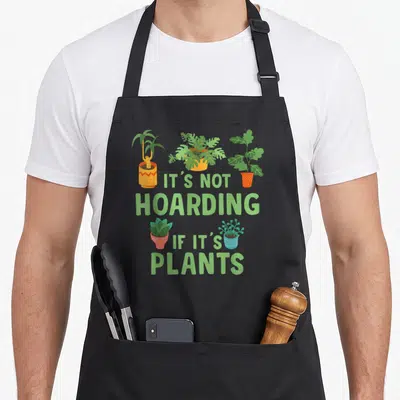 Tablier de cuisine noir avec cinq plantes en pot colorées et le texte It's Not Hoarding If It's Plants en vert.