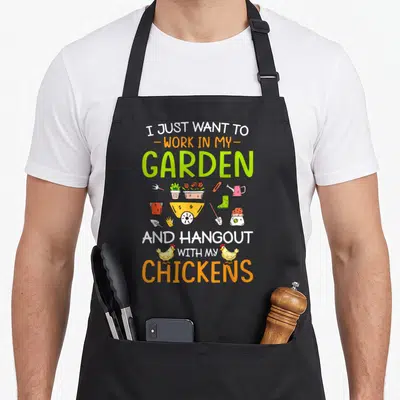 Tablier de cuisine noir avec illustration colorée d'un brouette, outils de jardinage et deux poules jaunes.