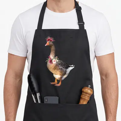 Tablier de cuisine noir avec illustration d'une oie portant une couronne de fleurs roses et rouges sur la tête et le cou.