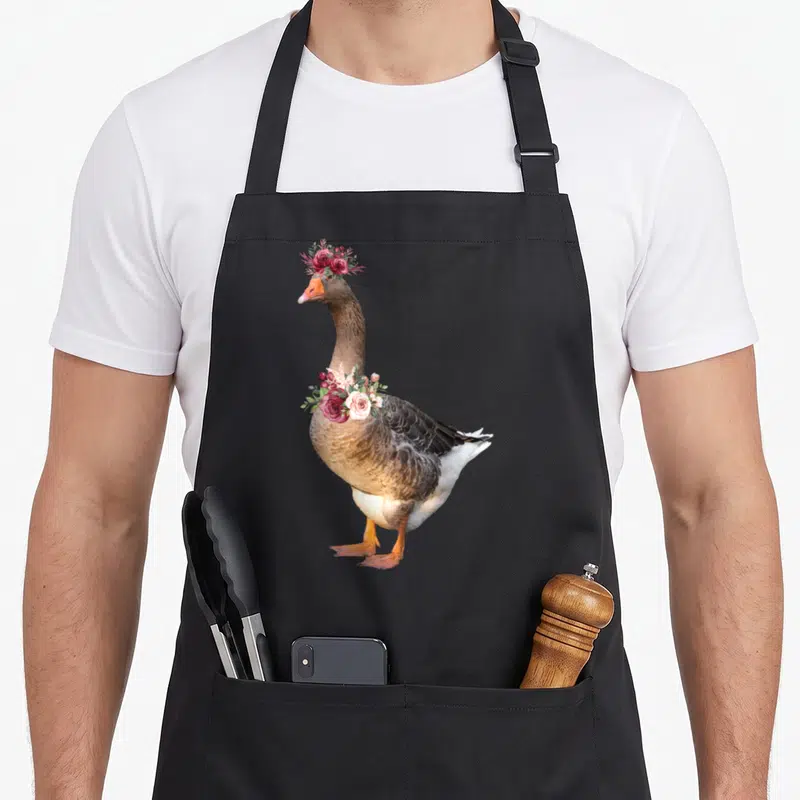 Tablier de cuisine noir avec illustration d'une oie portant une couronne de fleurs roses et rouges sur la tête et le cou.