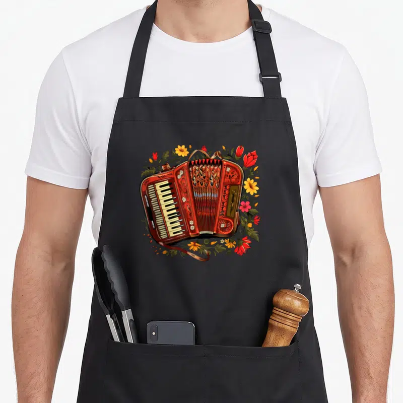 Tablier de cuisine noir avec accordéon rouge entouré de fleurs jaunes et roses aux feuilles vertes.