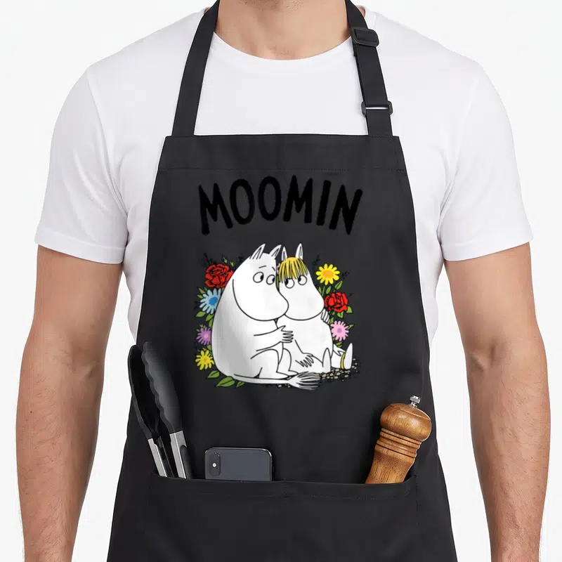 Tablier de cuisine noir avec Moomintroll et Snorkmaiden assis dans un bouquet de fleurs colorées sous le mot Moomin.